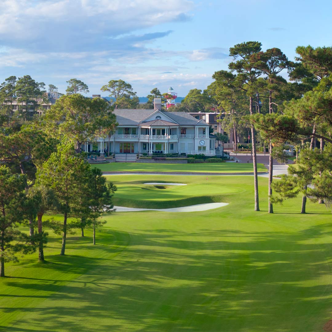 View of the 9th hole at Harbour Town Golf Links, featuring a manicured green, surrounding bunkers, and the iconic clubhouse framed by towering pines.
