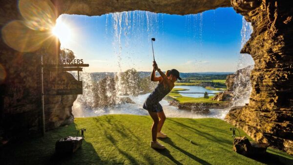 Ozarks golf at Cliffhangers Lion’s Den, featuring a golfer teeing off from a cave through a waterfall toward a scenic green in Branson, Missouri