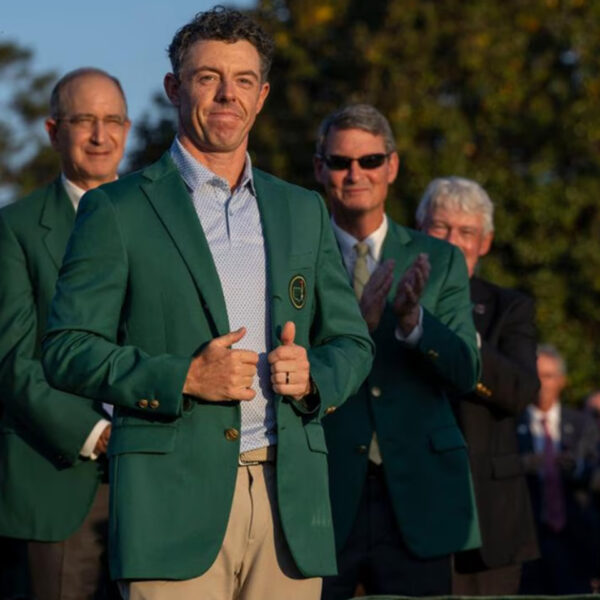 Rory McIlroy wearing the green jacket during the 2026 Masters champion ceremony at Augusta National, with officials applauding behind him.