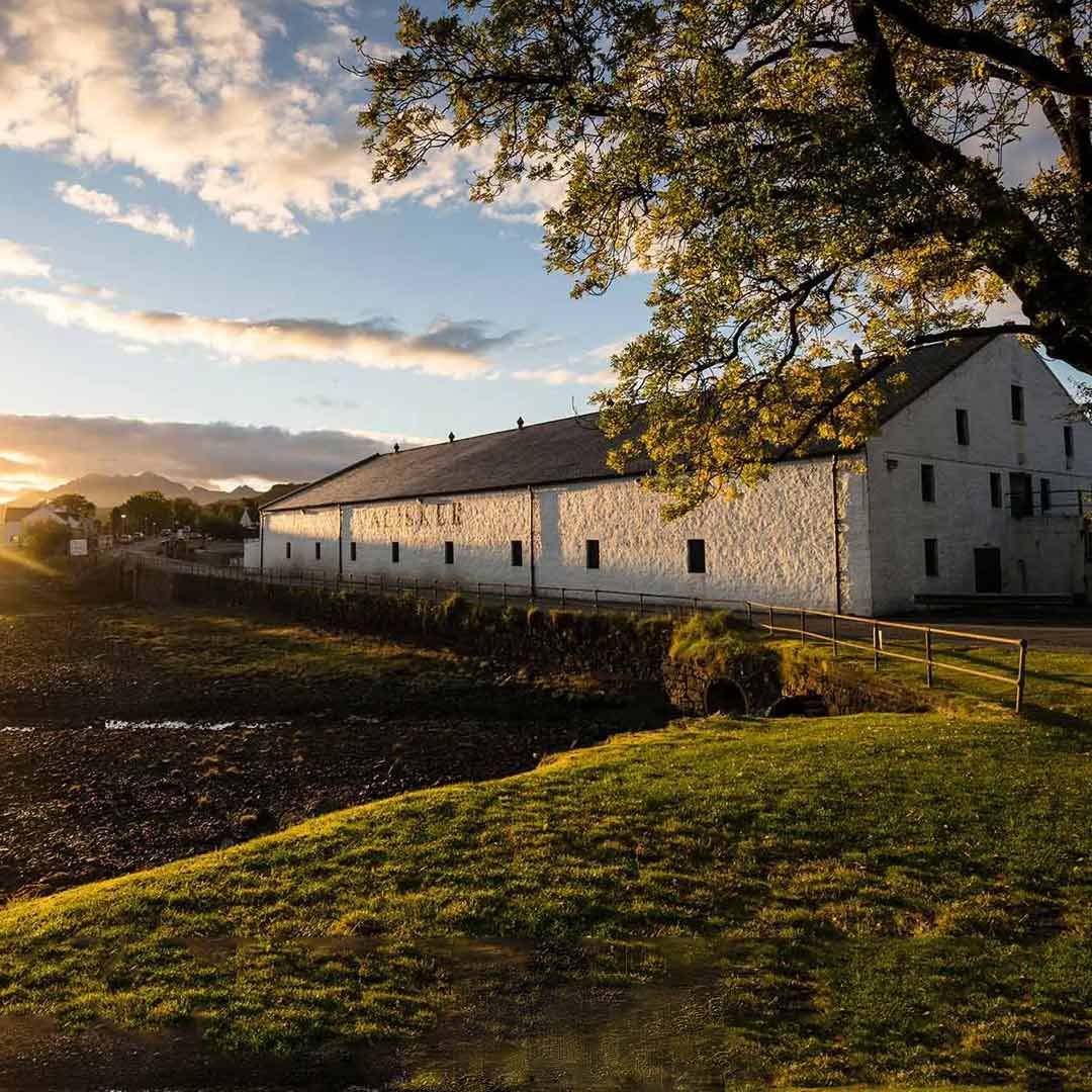 Talisker Distillery on the Isle of Skye at sunset, overlooking the rugged coastal landscape.